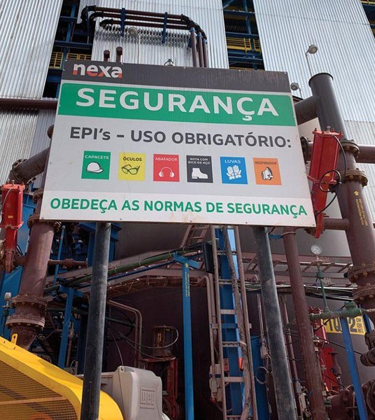Placa de segurança do trabalho instalada em planta industrial, indicando os EPIs de uso obrigatório